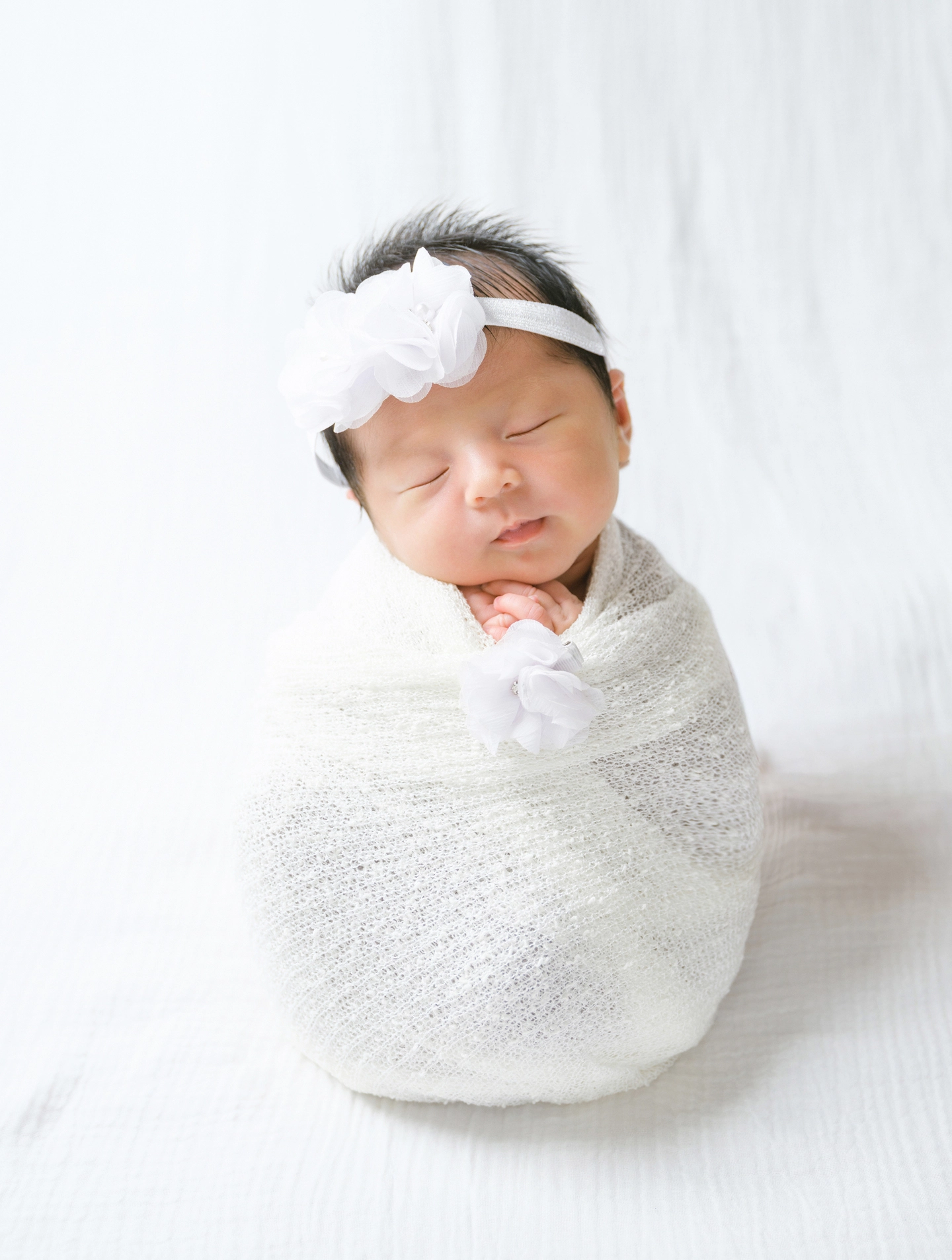 白い花のヘアバンドとおくるみで眠る赤ちゃん