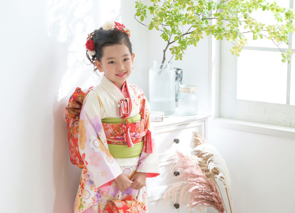 窓辺で花柄の着物と帯を身につけた七五三の女の子