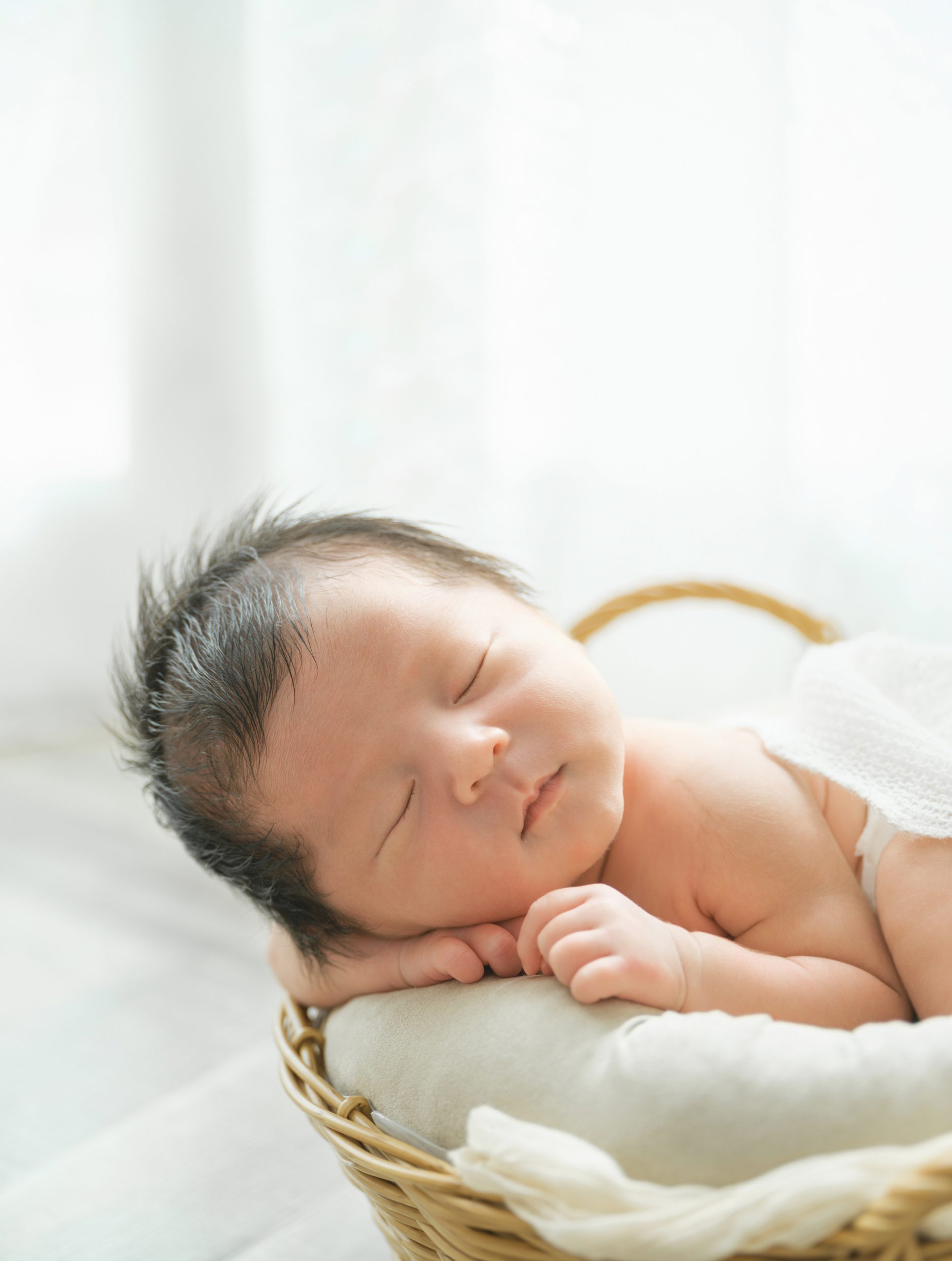 白い布を敷いたかごの中で眠る、生まれたばかりの赤ちゃん