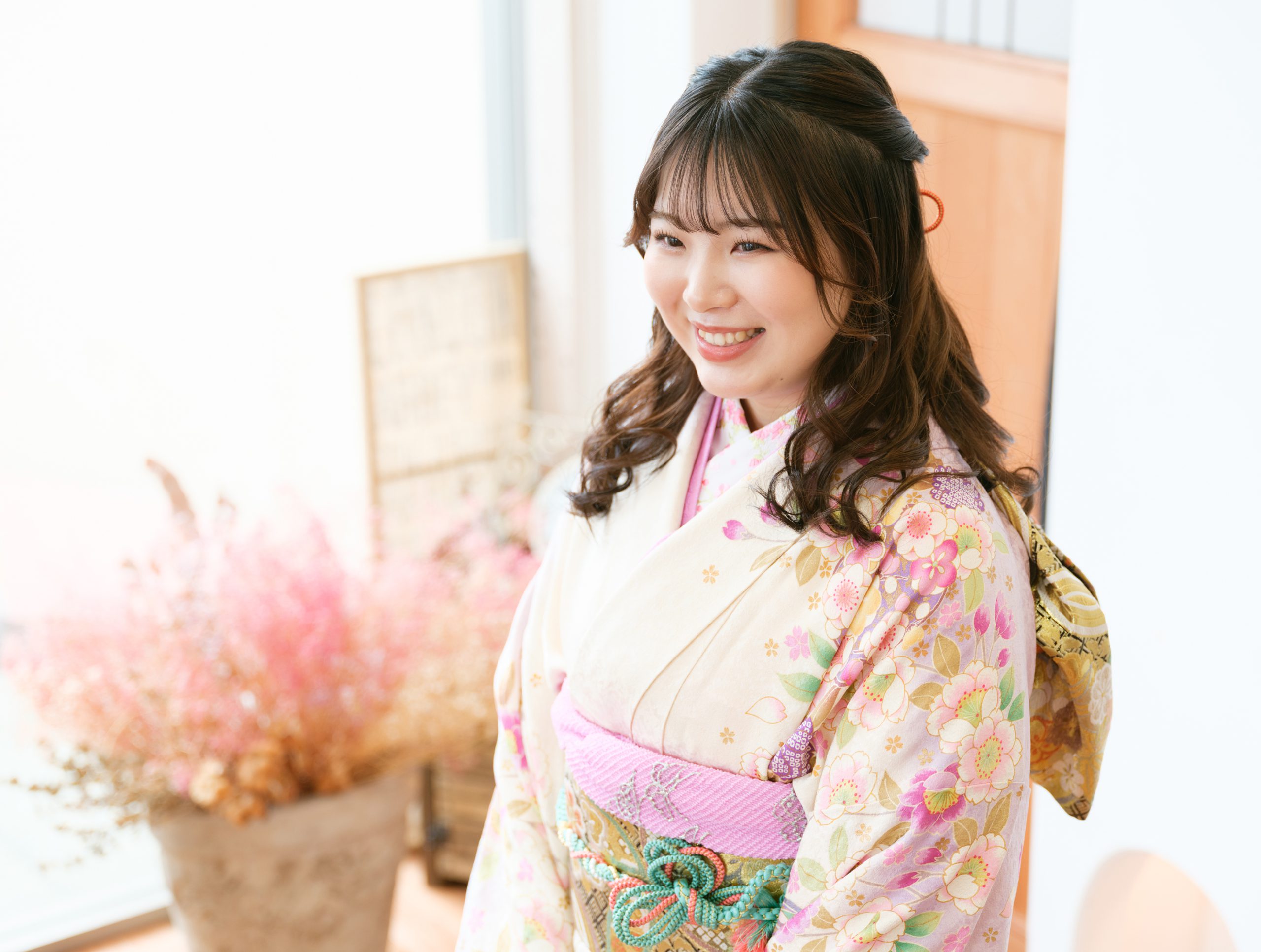 淡い色の振袖を着て、花を背景にほほえむ成人記念写真